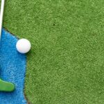 Mini-golf clubs and balls of different colors laid on artificial grass.