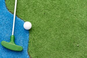 Mini-golf clubs and balls of different colors laid on artificial grass.