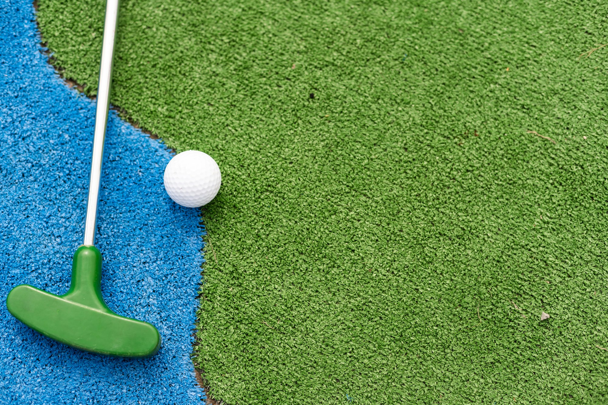 Mini-golf clubs and balls of different colors laid on artificial grass.